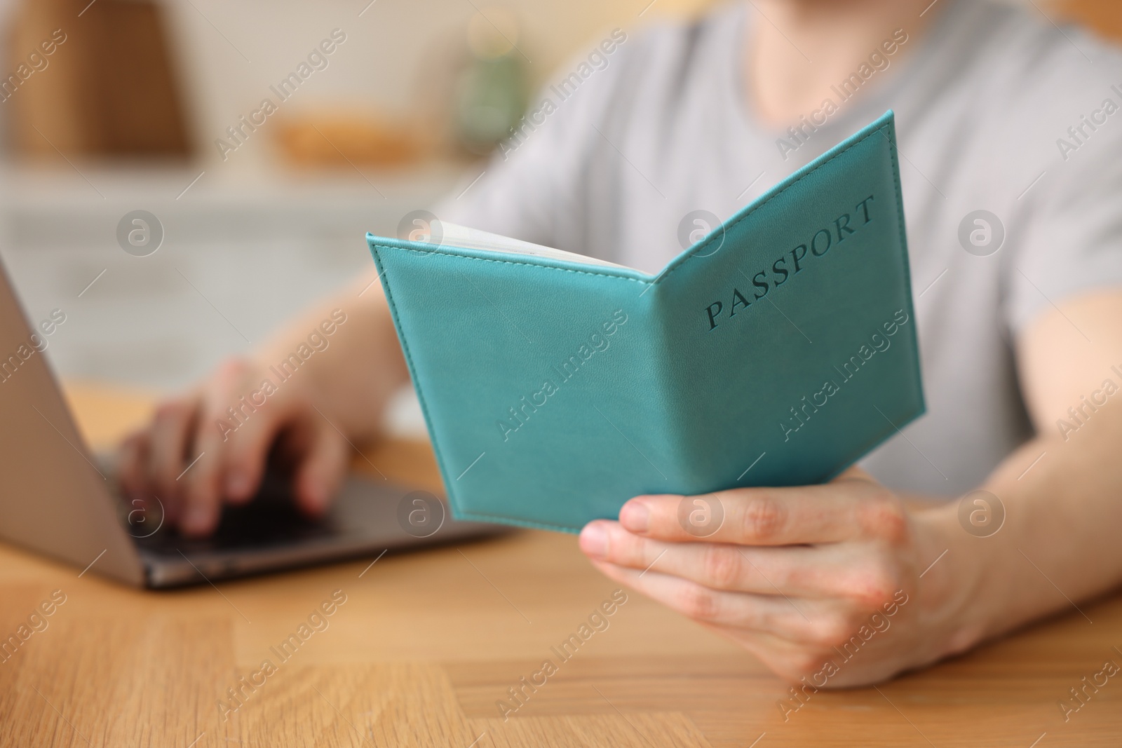 Man with passport using laptop at wooden table indoors, closeup Photo of Man with passport using laptop at wooden table indoors, closeup