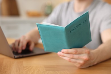 Photo of Man with passport using laptop at wooden table indoors, closeup