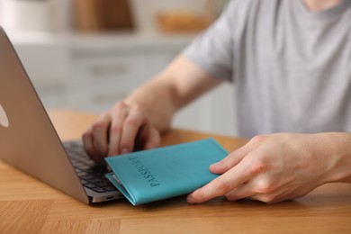 Photo of Man with passport using laptop at wooden table indoors, closeup