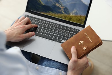 Photo of Man with passport using laptop at table indoors, closeup