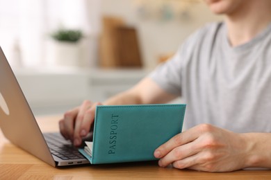 Photo of Man with passport using laptop at wooden table indoors, closeup