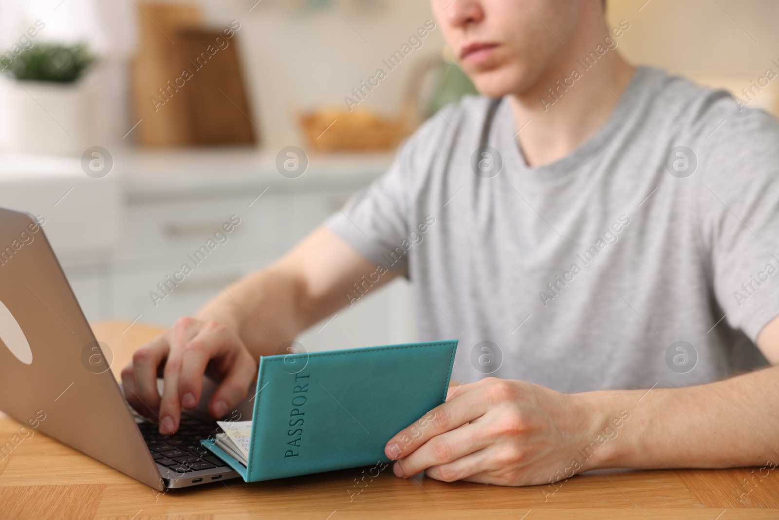Man with passport using laptop at wooden table indoors, closeup Photo of Man with passport using laptop at wooden table indoors, closeup