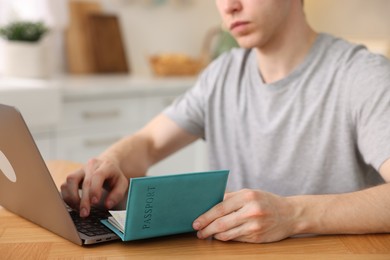 Photo of Man with passport using laptop at wooden table indoors, closeup