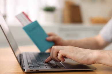 Photo of Man with passport and flight ticket using laptop at table indoors, closeup