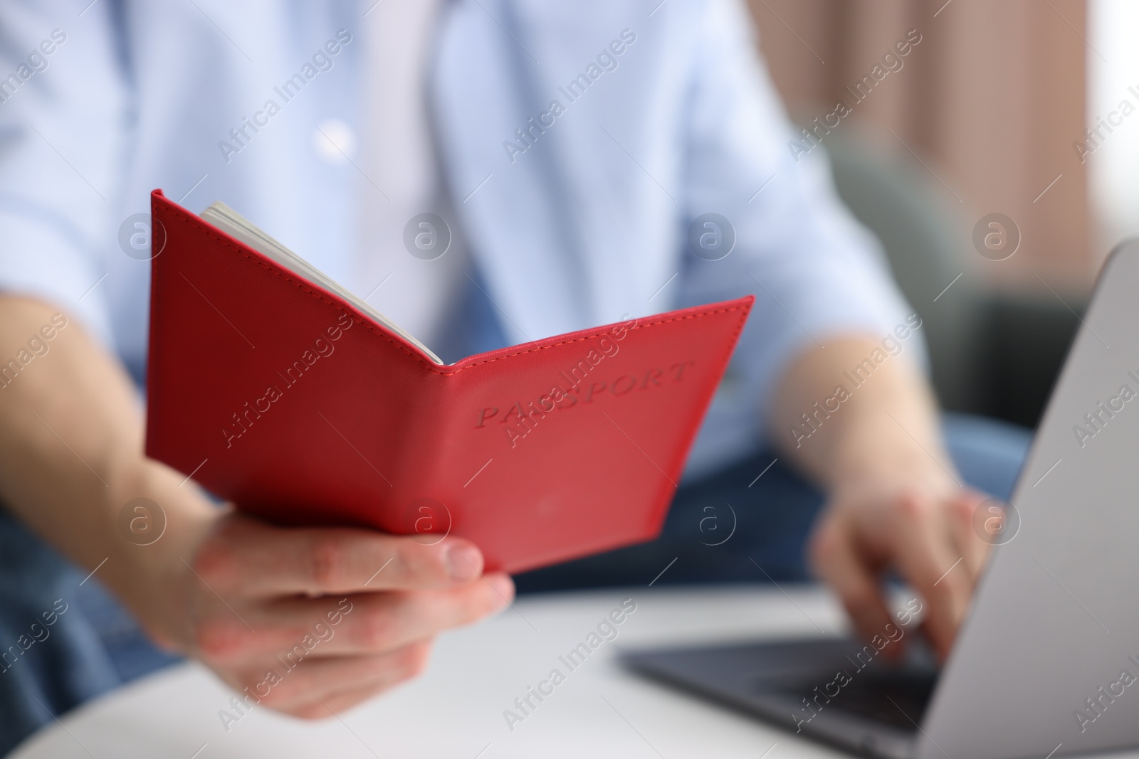 Man with passport using laptop at table indoors, closeup Photo of Man with passport using laptop at table indoors, closeup