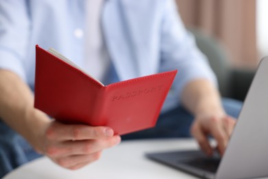 Photo of Man with passport using laptop at table indoors, closeup