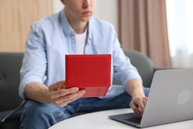 Photo of Man with passport using laptop at table indoors, closeup