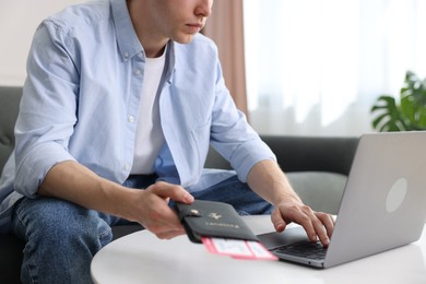 Photo of Man with passport and flight tickets using laptop at table indoors, closeup