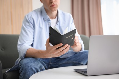Photo of Man with passport near laptop at home, closeup