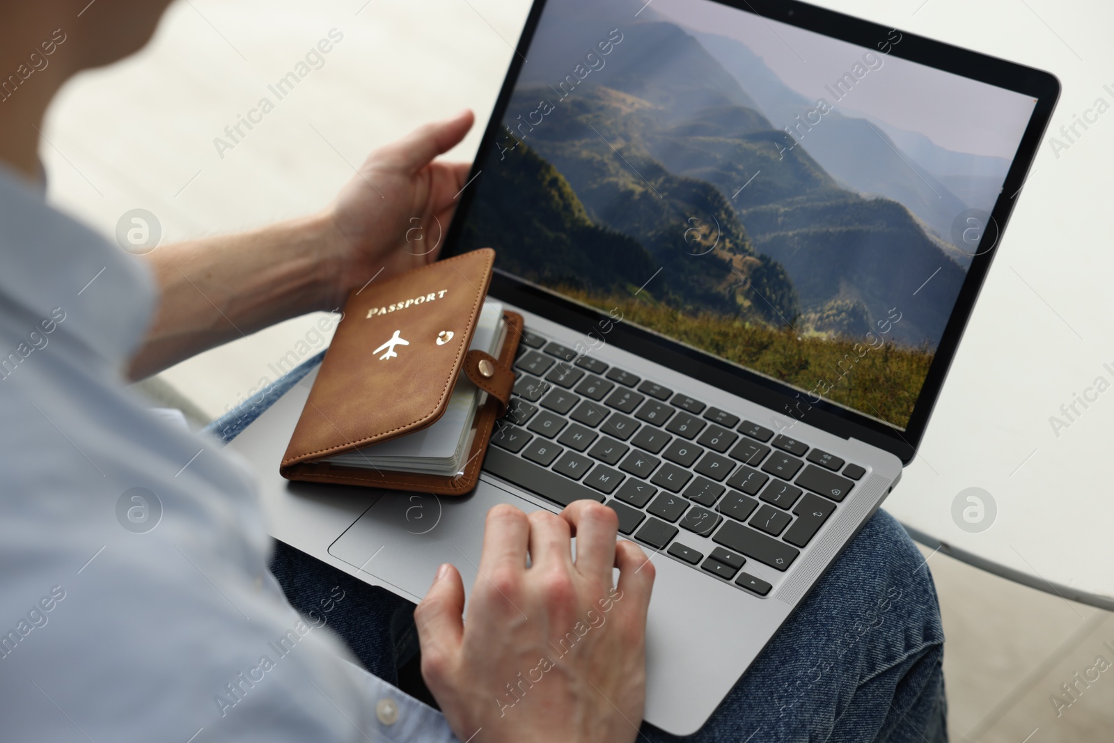 Man with passport using laptop at table indoors, closeup Photo of Man with passport using laptop at table indoors, closeup