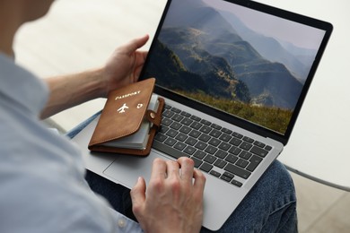Photo of Man with passport using laptop at table indoors, closeup