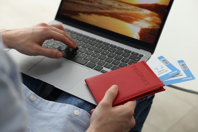 Photo of Man with passport and flight tickets using laptop at table indoors, closeup