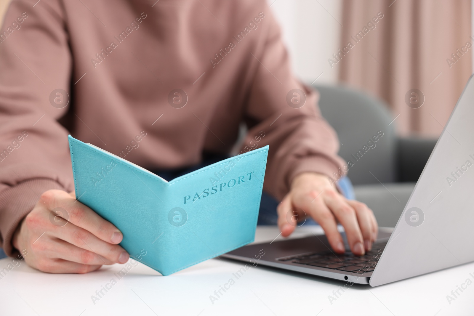 Man with passport using laptop at table indoors, closeup Photo of Man with passport using laptop at table indoors, closeup
