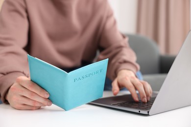 Photo of Man with passport using laptop at table indoors, closeup