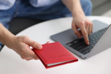 Photo of Man with passport using laptop at table indoors, closeup