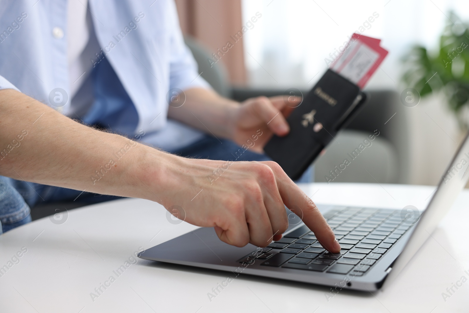 Man with passport and flight tickets using laptop at table indoors, closeup Photo of Man with passport and flight tickets using laptop at table indoors, closeup
