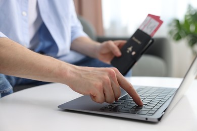 Photo of Man with passport and flight tickets using laptop at table indoors, closeup