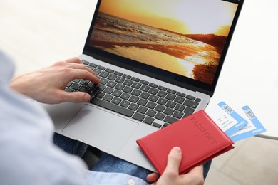 Photo of Man with passport and flight tickets using laptop at table indoors, closeup