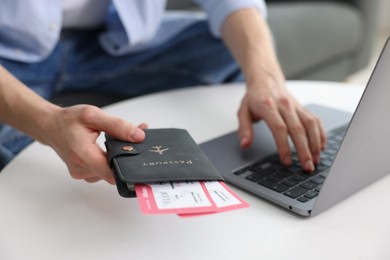 Photo of Man with passport and flight tickets using laptop at table indoors, closeup