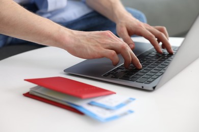 Photo of Man using laptop at table with passport and flight tickets indoors, closeup