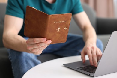 Photo of Man with passport using laptop at table indoors, closeup