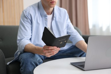 Photo of Man with passport using laptop at table indoors, closeup
