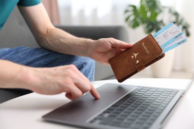 Photo of Man with passport and flight tickets using laptop at table indoors, closeup