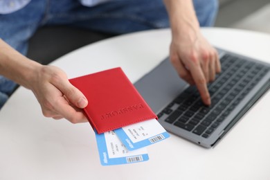 Photo of Man with passport and flight tickets using laptop at table indoors, closeup