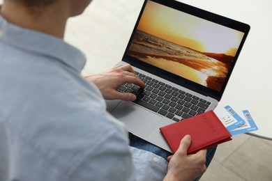 Photo of Man with passport and flight tickets using laptop at table indoors, closeup