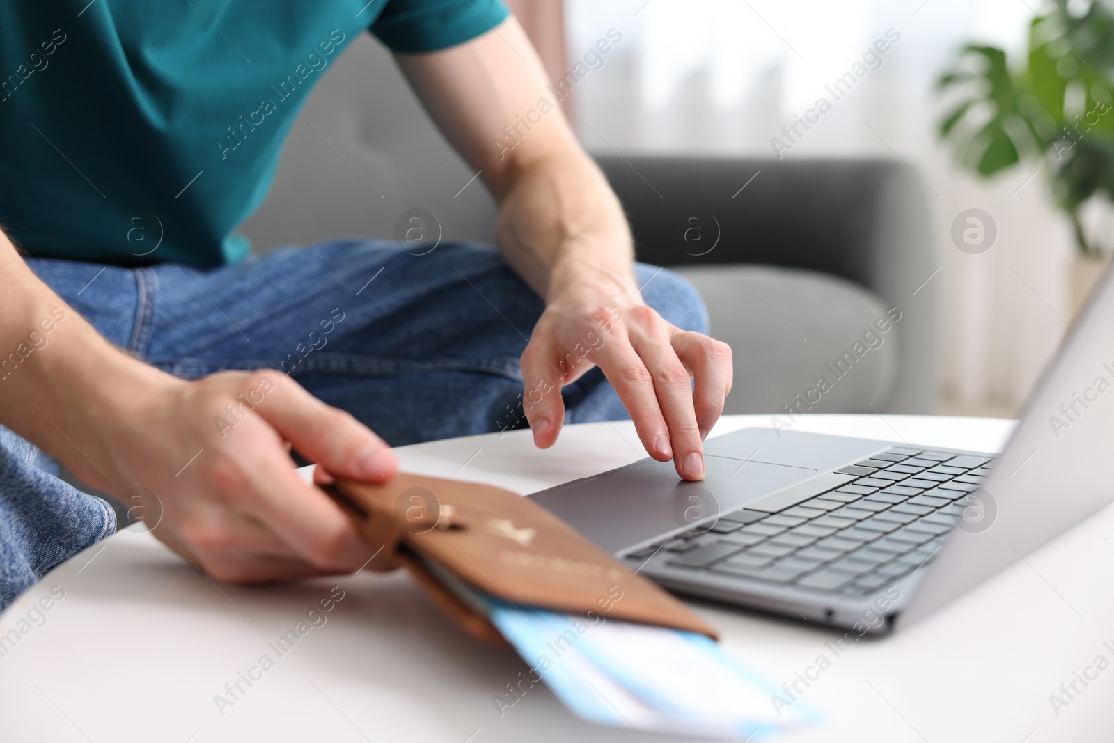 Man with passport and flight tickets using laptop at table indoors, closeup Photo of Man with passport and flight tickets using laptop at table indoors, closeup