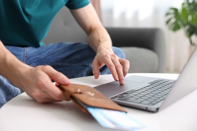 Photo of Man with passport and flight tickets using laptop at table indoors, closeup