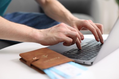 Photo of Man using laptop at table with passport and flight tickets indoors, closeup
