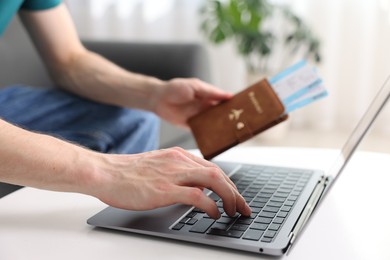 Photo of Man with passport and flight tickets using laptop at table indoors, closeup