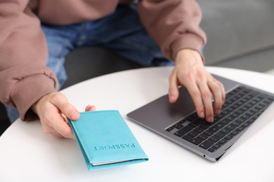 Photo of Man with passport using laptop at table indoors, closeup