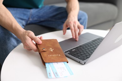 Photo of Man with passport and flight tickets using laptop at table indoors, closeup