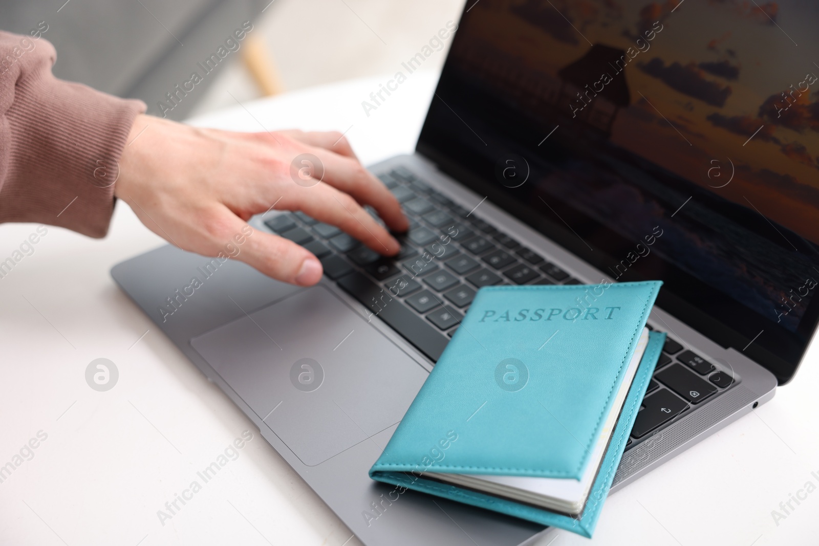 Man with passport using laptop at table indoors, closeup Photo of Man with passport using laptop at table indoors, closeup