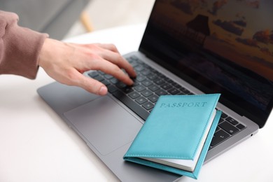 Photo of Man with passport using laptop at table indoors, closeup