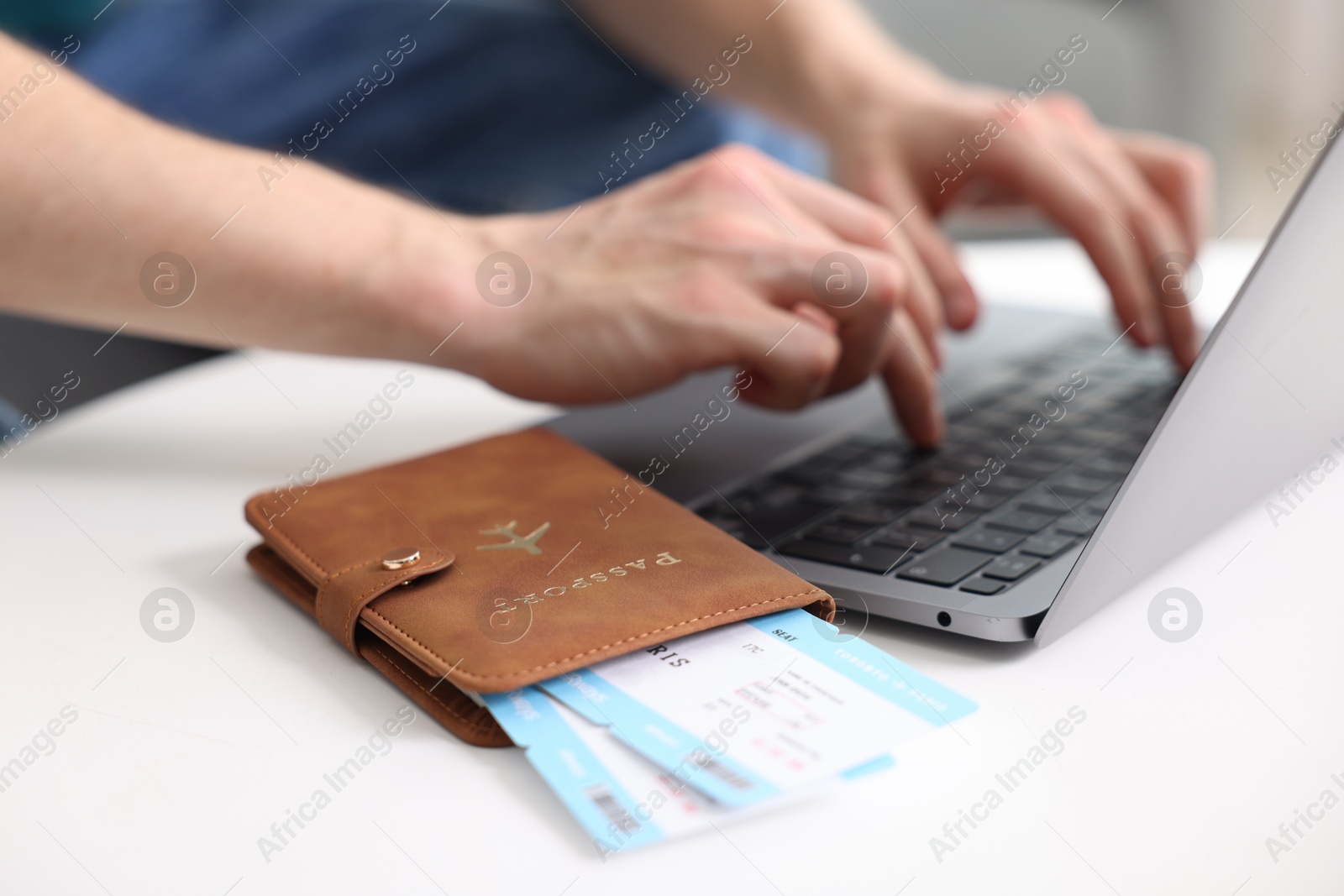 Man using laptop at table with passport and flight tickets indoors, closeup Photo of Man using laptop at table with passport and flight tickets indoors, closeup