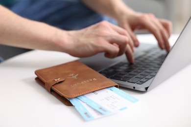 Photo of Man using laptop at table with passport and flight tickets indoors, closeup