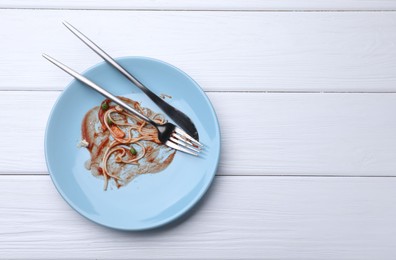 Photo of Dirty plate with spaghetti, peas, tomato sauce and cutlery on white wooden table, top view. Space for text