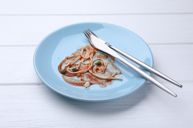 Photo of Dirty plate with spaghetti, peas, tomato sauce and cutlery on white wooden table, closeup