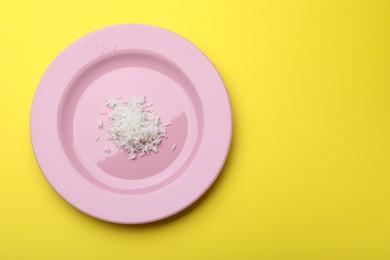 Photo of Plate with cooked rice on yellow background, top view. Space for text