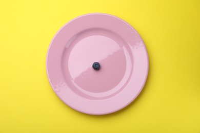 Photo of Plate with fresh blueberry on yellow background, top view