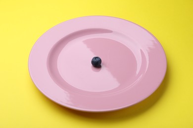 Photo of Plate with fresh blueberry on yellow background, closeup
