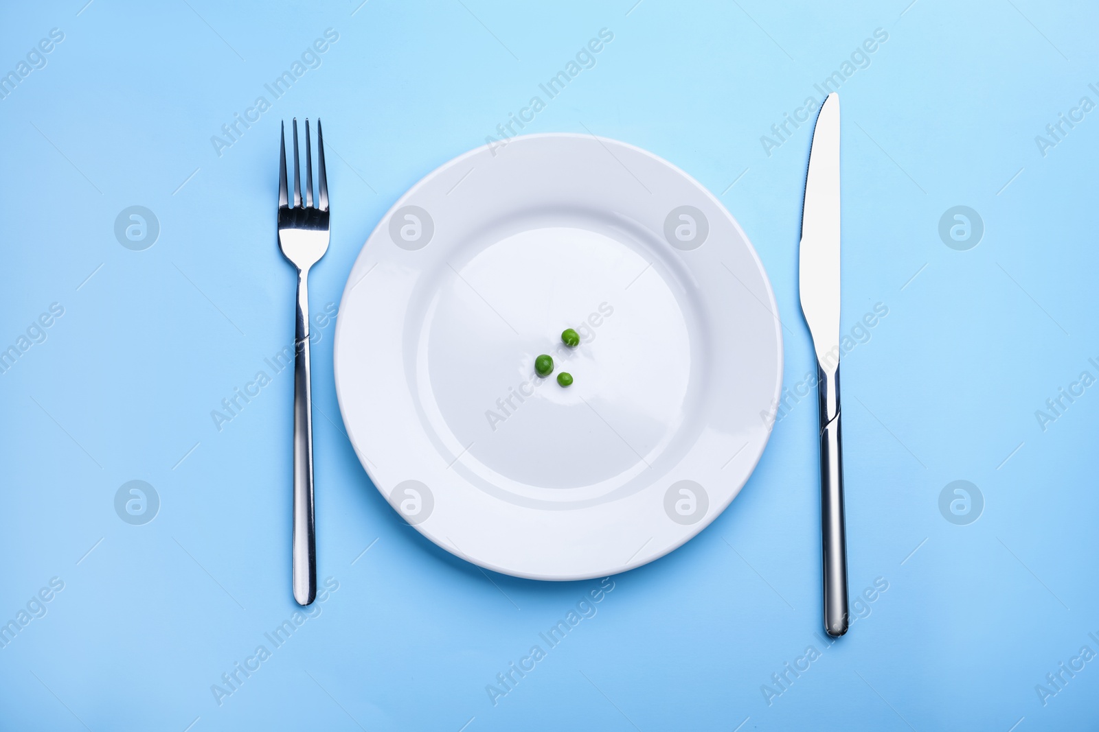 Plate with fresh green peas and cutlery on light blue background, top view Photo of Plate with fresh green peas and cutlery on light blue background, top view