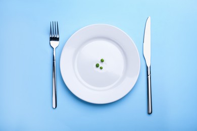 Photo of Plate with fresh green peas and cutlery on light blue background, top view