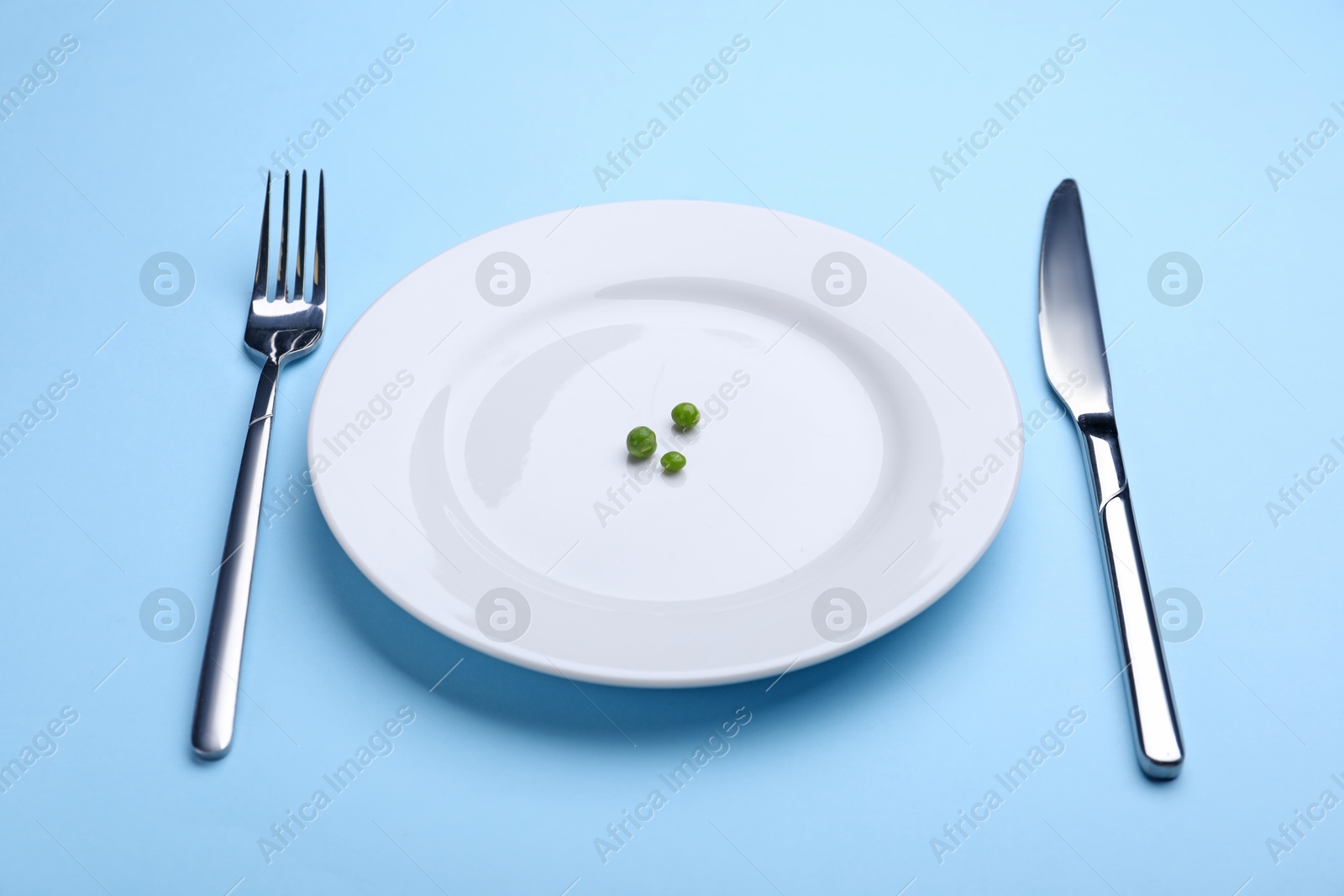 Plate with fresh green peas and cutlery on light blue background, closeup Photo of Plate with fresh green peas and cutlery on light blue background, closeup