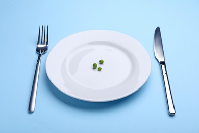 Photo of Plate with fresh green peas and cutlery on light blue background, closeup
