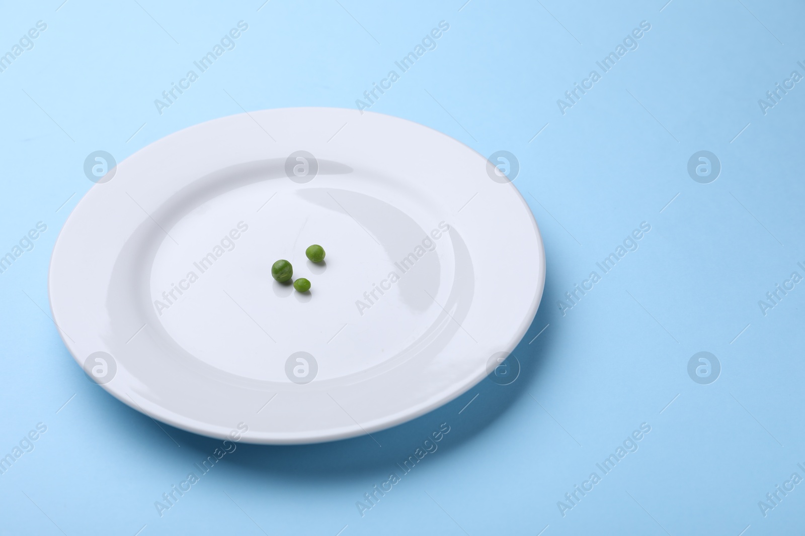 Plate with fresh green peas on light blue background, closeup. Space for text Photo of Plate with fresh green peas on light blue background, closeup. Space for text