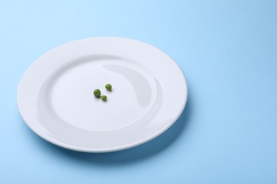 Photo of Plate with fresh green peas on light blue background, closeup. Space for text
